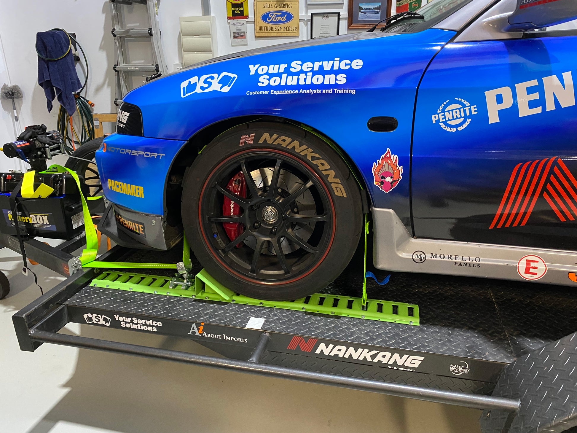 Blue car on a lift in a garage with various branding and logos.